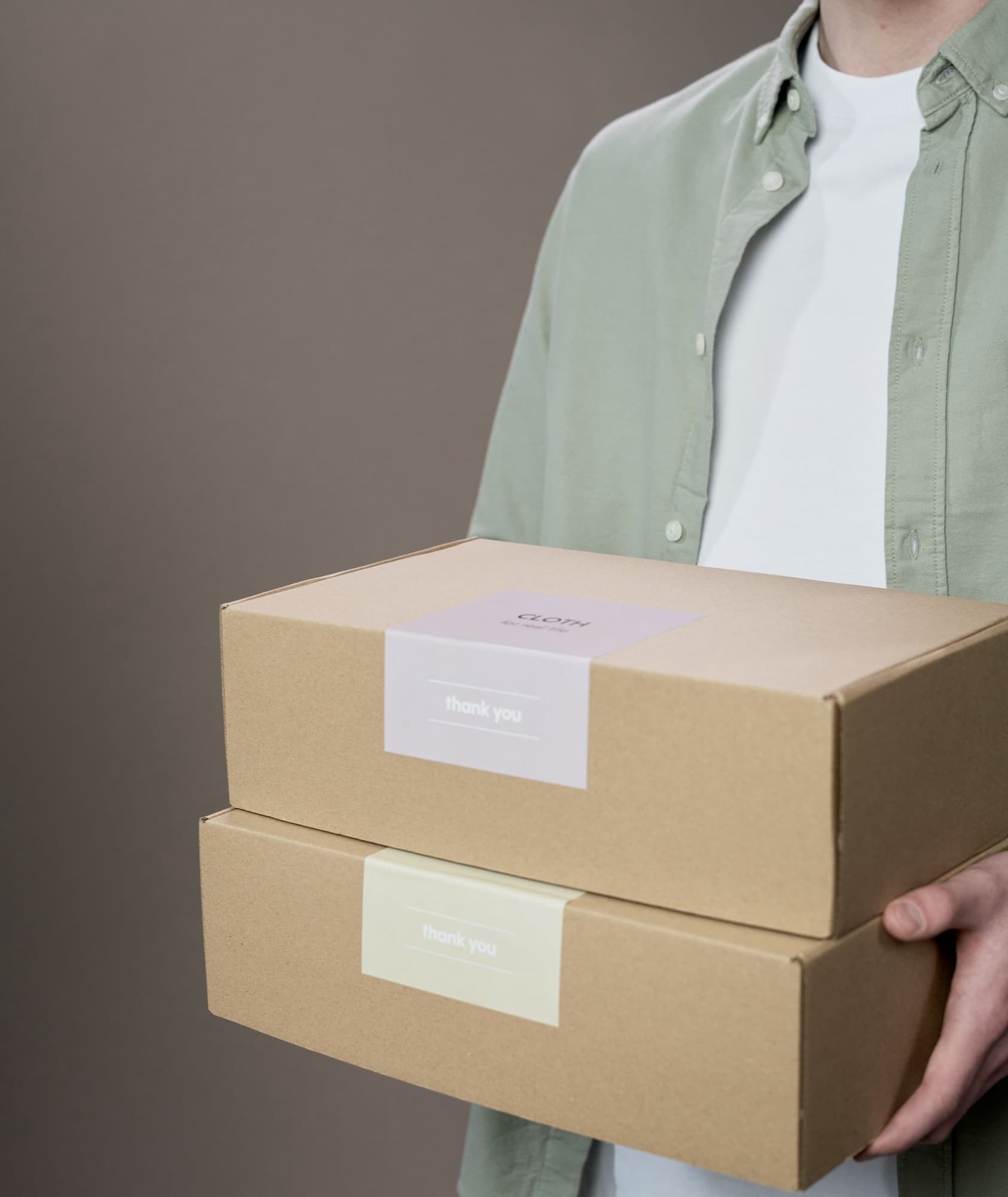 Person in a sage green shirt holding two labelled kraft parcels, ready to send