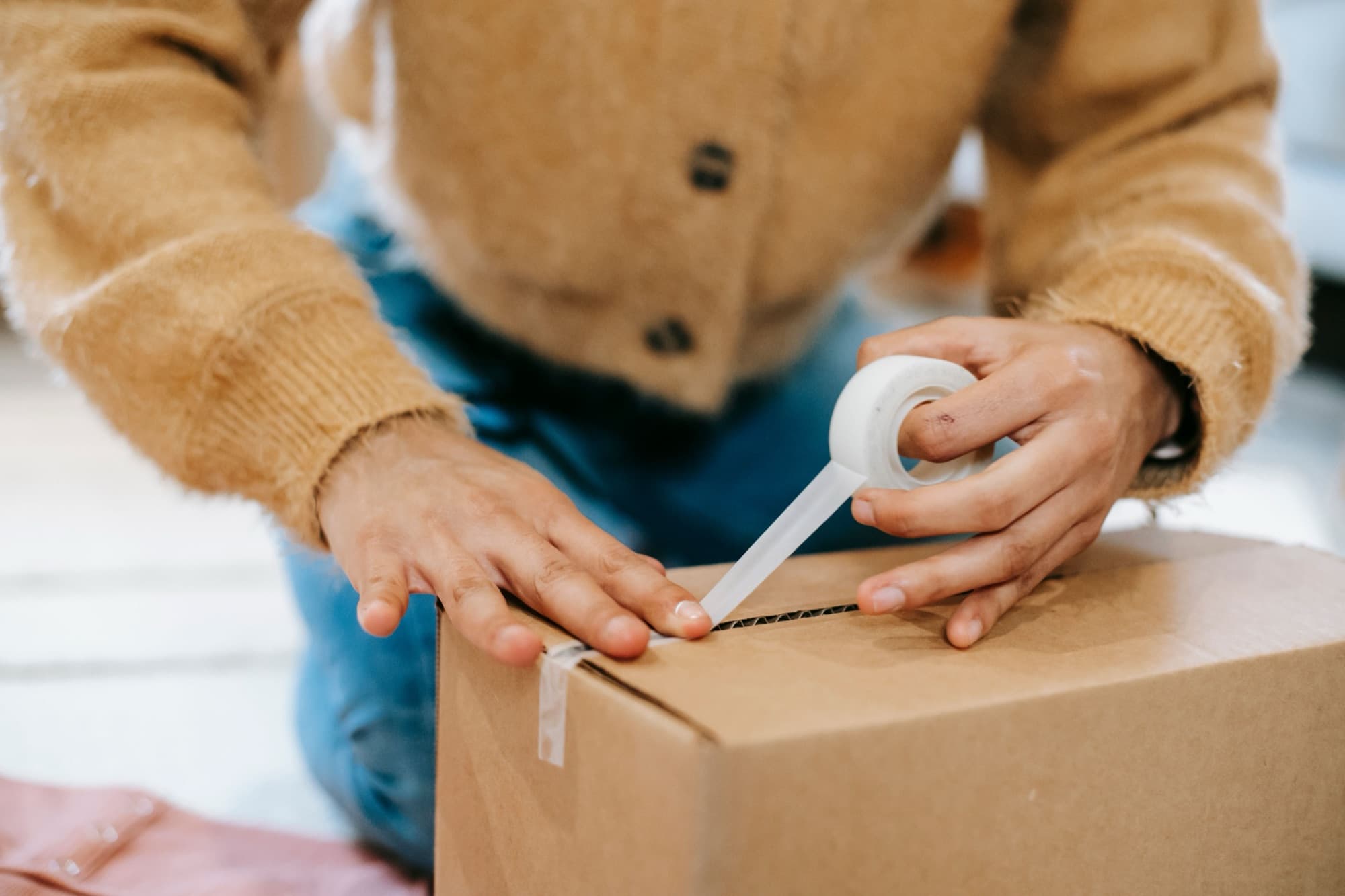 Hands running a tape gun along the seam of a cardboard box